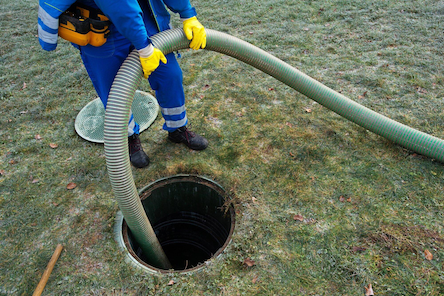 Man feeds tube into hole in ground as part of septic cleaning service